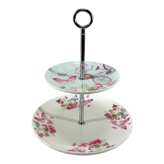 This is a 2-tier porcelain afternoon tea cake stand featuring a vintage-style floral design with pink roses, butterflies, and a whimsical bicycle with a flower basket. Vintage inspired very pretty centerpiece for serving pastries, cupcakes, or finger sandwiches during high tea. 2-Tier Cake Stand with a center tier rod and carry ring. Rockhampton Vintage Hire Wedding, Event, Party Hire