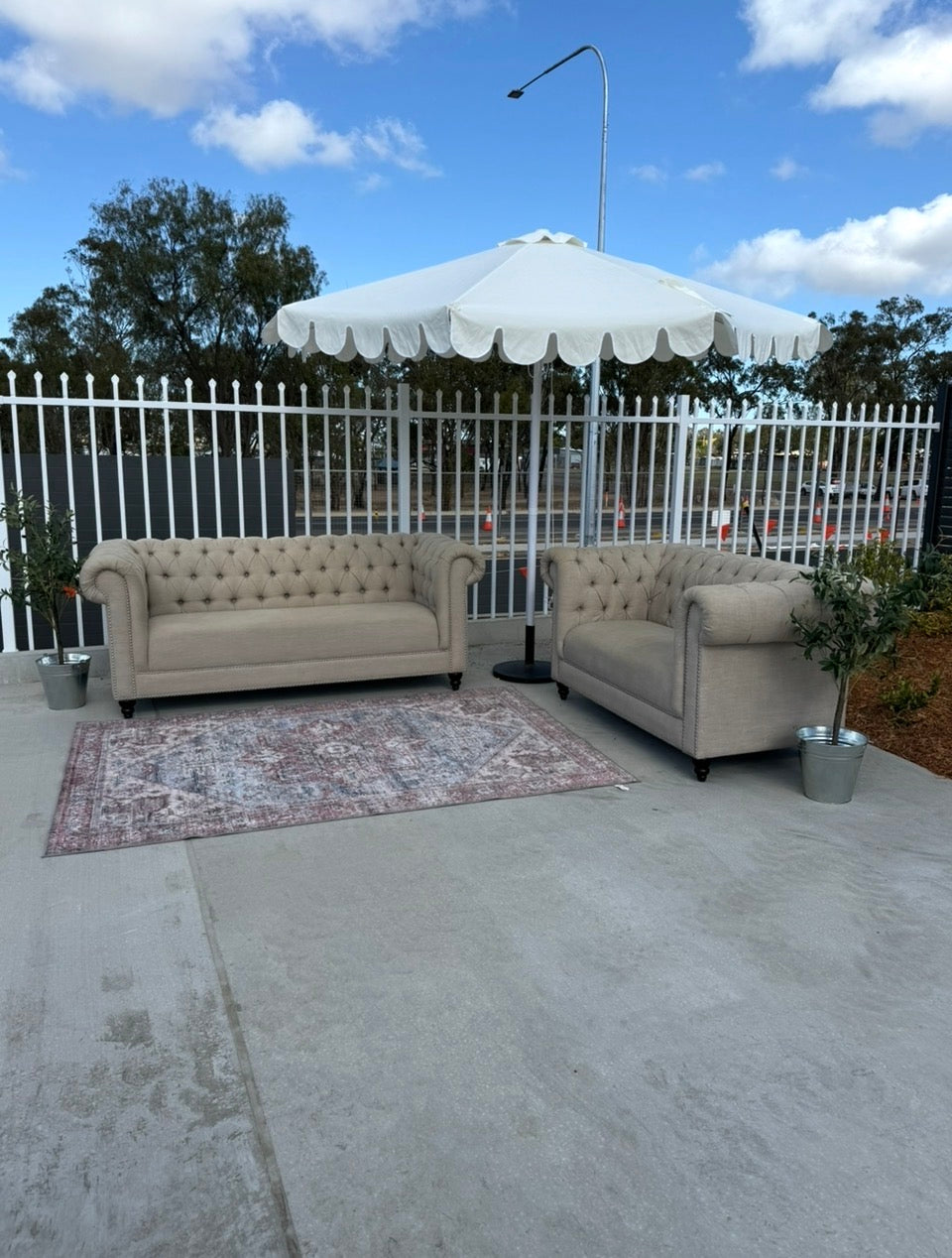 Rockhampton Vintage Hire wedding & event seating set up featuring 2 x linen beige Chesterfield lounges, a patterned vintage look area rug, a scalloped white market umbrella and olive trees. Rockhampton Weddings, events and parties